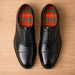 Black dress shoes with red plaid foam insoles on a wooden surface
