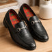 Black leather loafers with plaid insoles and a silver buckle on a wooden surface.