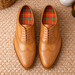 Pair of brown leather shoes with plaid lining on a textured surface